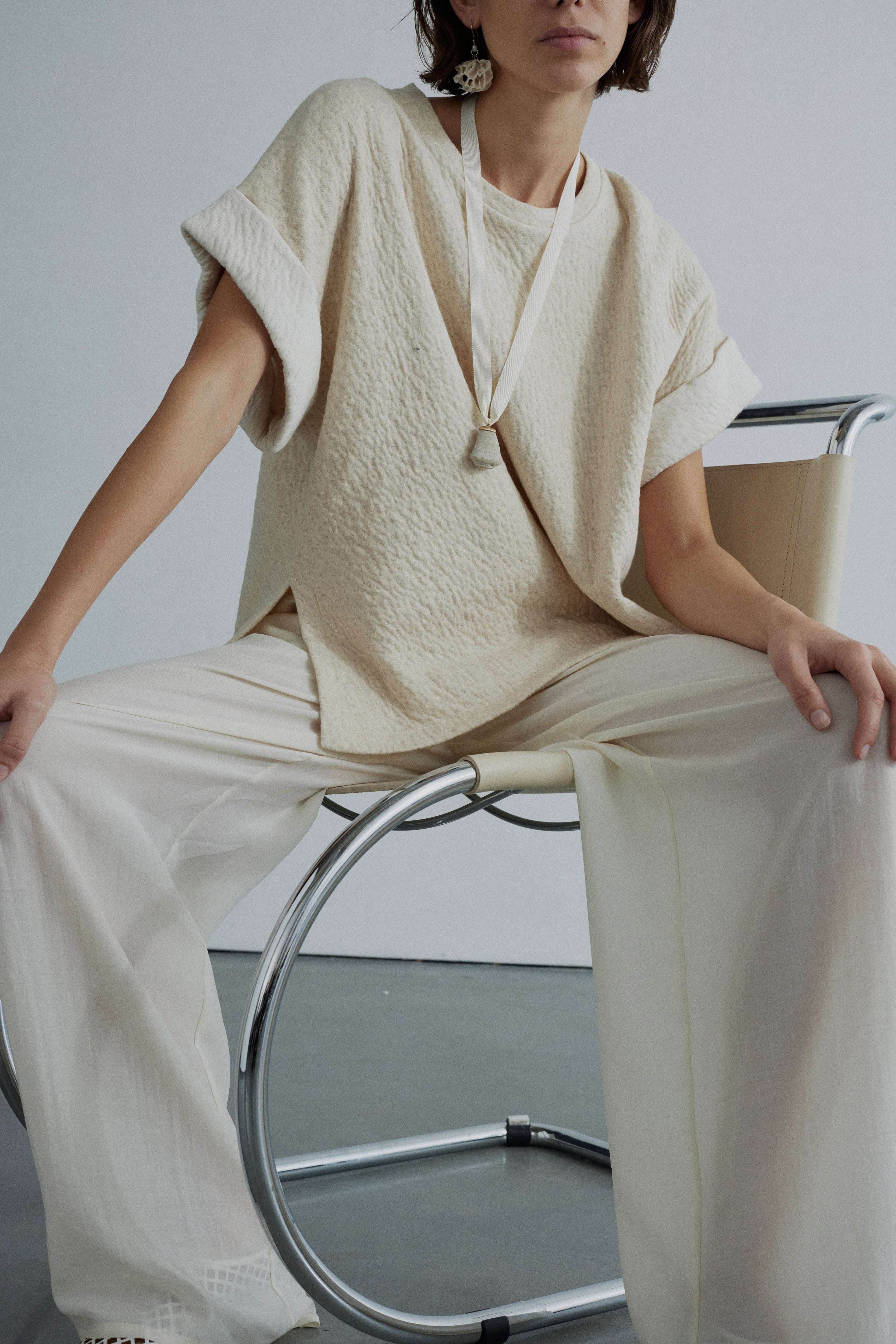 Person wearing a beige textured top and pants sitting on a modern chair.